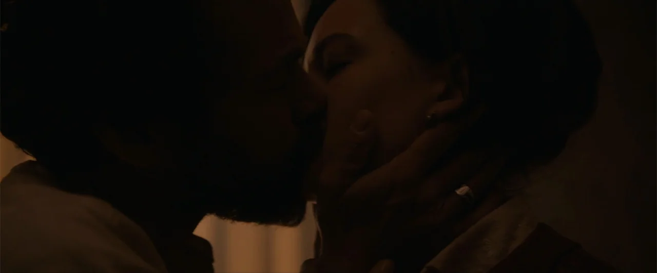 Eiffel (2021) movie still: closeup — A dimly lit interior room with soft shadows on the subjects' faces. A man and a woman lean into each other and…