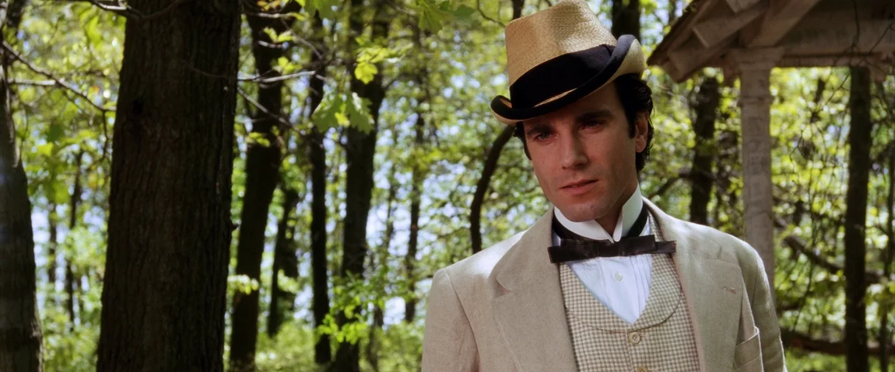 The Age of Innocence (1993) movie still: medium — A lush, sunlit forest backdrop with thick tree trunks and dense green leaves overhead. A man…