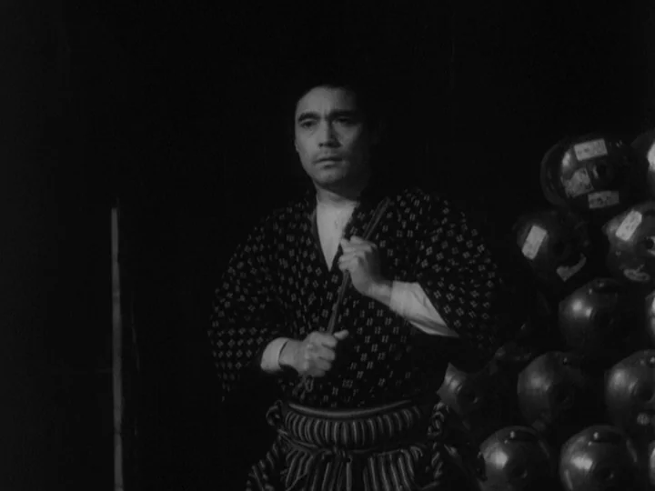 Sanshiro Sugata (1943) movie still: medium — A dark, dimly lit cellar with stacks of rounded storage vessels in the background. A man stands in the…