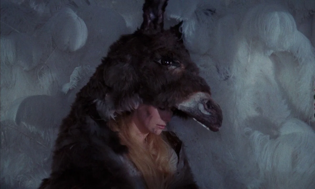 Donkey Skin (1970) movie still: medium — A figure sits surrounded by a wall of textured white ostrich feathers. The subject wears a dark brown…
