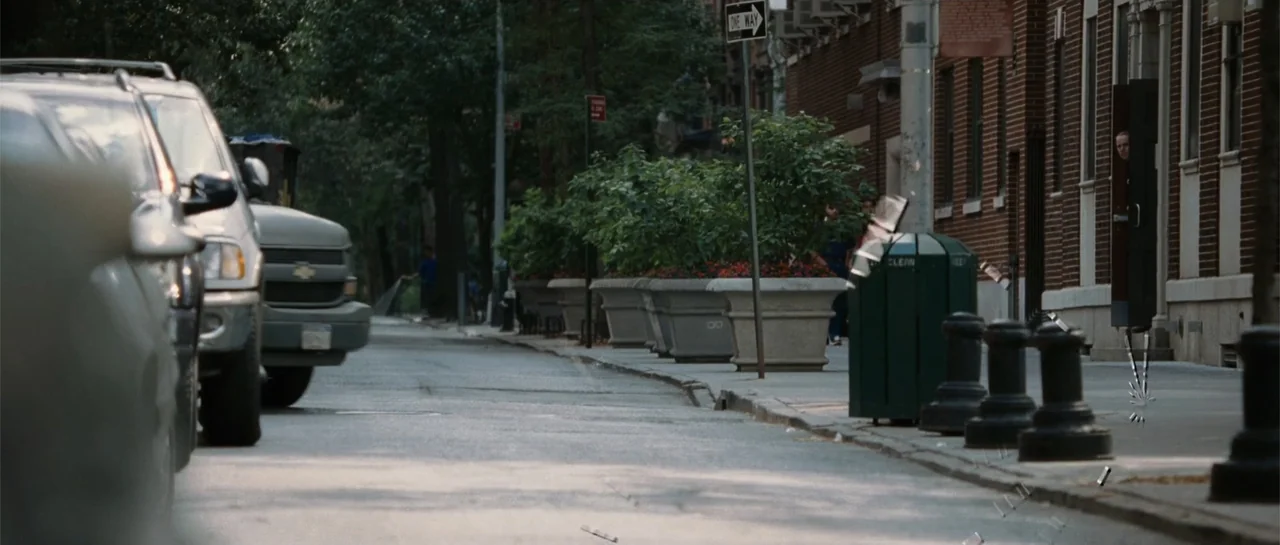 Inside Man (2006) movie still: wide — A quiet urban street lined with parked vehicles and large concrete planter boxes. The sidewalk runs parallel…