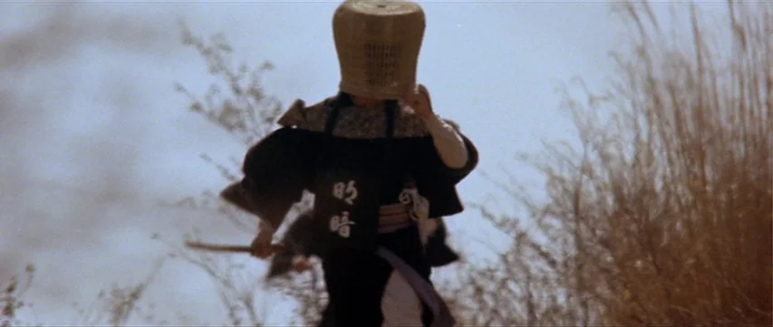 Lone Wolf: Baby Cart at the River Styx (1972) movie still: fullbody — A figure walks through tall dry grass in an open outdoor area. The person…