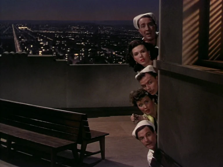 On The Town (1949) movie still: medium — A dark outdoor terrace overlooking a distant illuminated city skyline at night. Five people in naval-style…