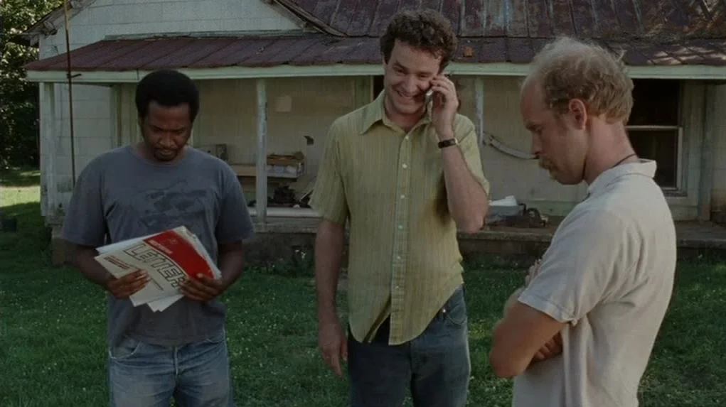 Junebug (2005) movie still: fullbody — Three men stand in the front yard of a weathered house with peeling paint. They are engaged in an informal…