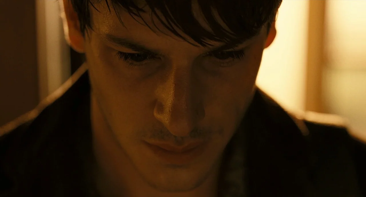 It’s Only The End Of The World (2016) movie still: closeup — A man stands in a dark, dimly lit interior environment. He gazes downward with his hair…