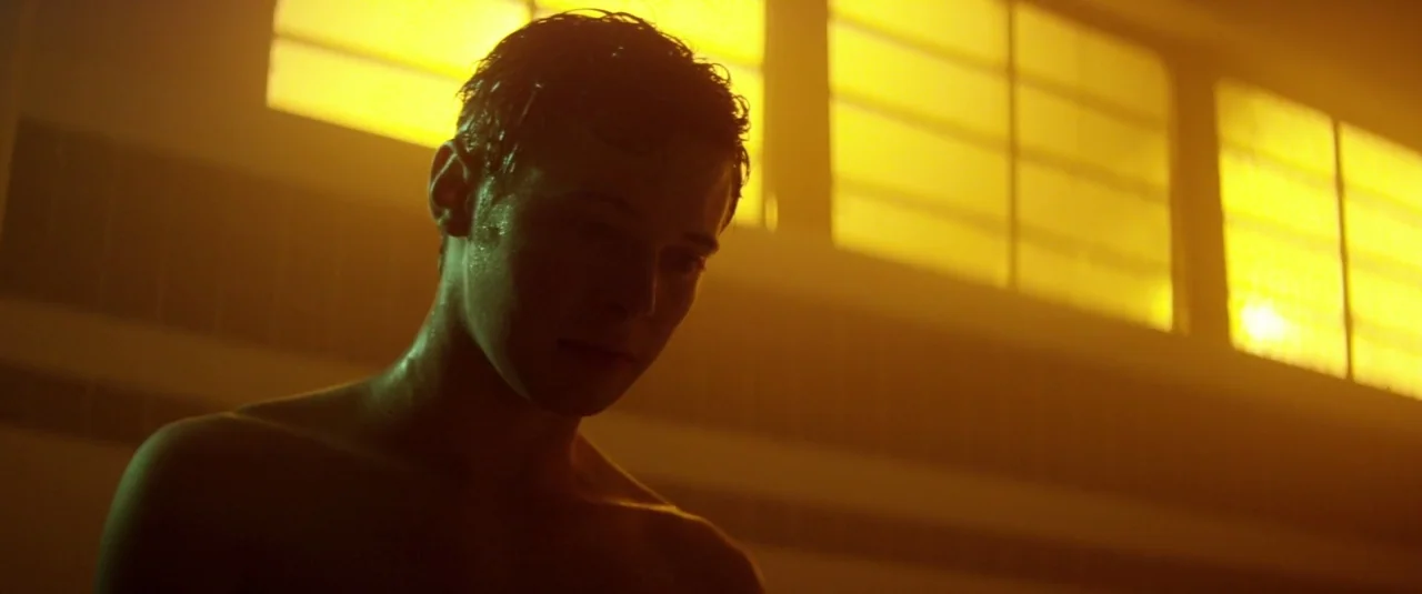Officer Downe (2016) movie still: medium — A tiled room with high rectangular windows glows with intense yellow natural light. A young man with wet…
