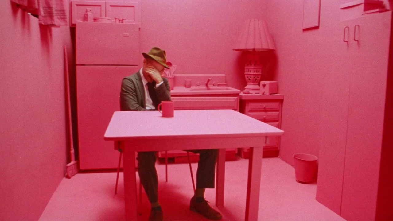 Strawberry Mansion (2021) movie still: medium — A square room furnished with domestic appliances and furniture, all painted a solid pink. A man in a…
