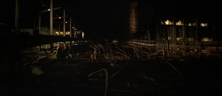 All The Real Girls (2003) movie still: wide — A dark, dilapidated industrial site features rusted metal framing and skeletal dead vegetation. A…