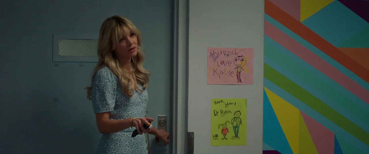 Promising Young Woman (2020) movie still: medium — A clinical hallway features a light blue door and colorful wall geometry decoration. A woman in a…