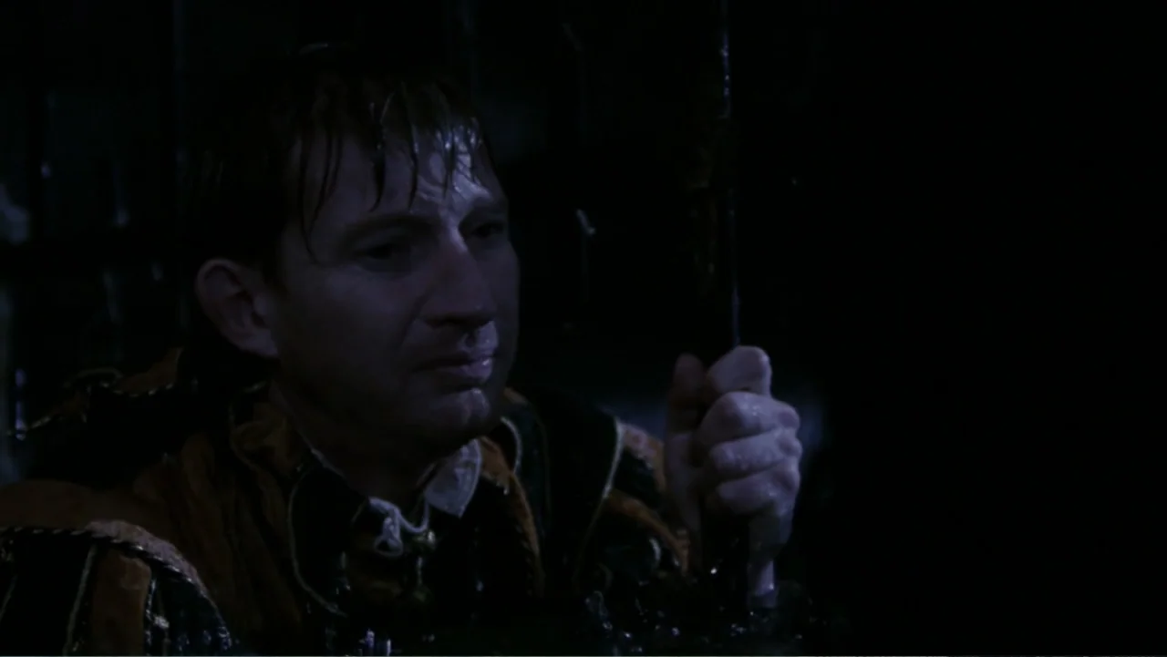 Van Helsing (2004) movie still: closeup — A man stands within a dark stone chamber behind iron prison bars. He grips the cold metal bar tightly…