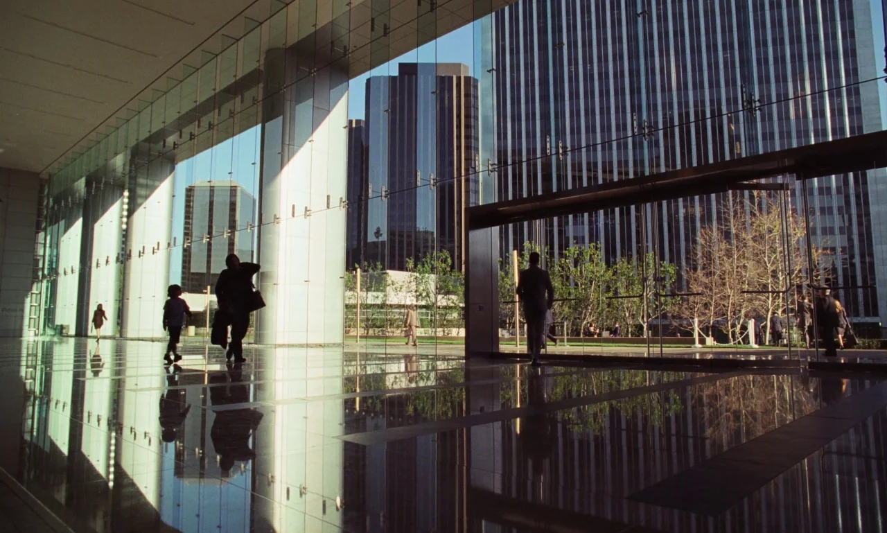 Marriage Story movie still: wide — A modern lobby with floor-to-ceiling glass walls overlooks a high-rise city business district. Several people…