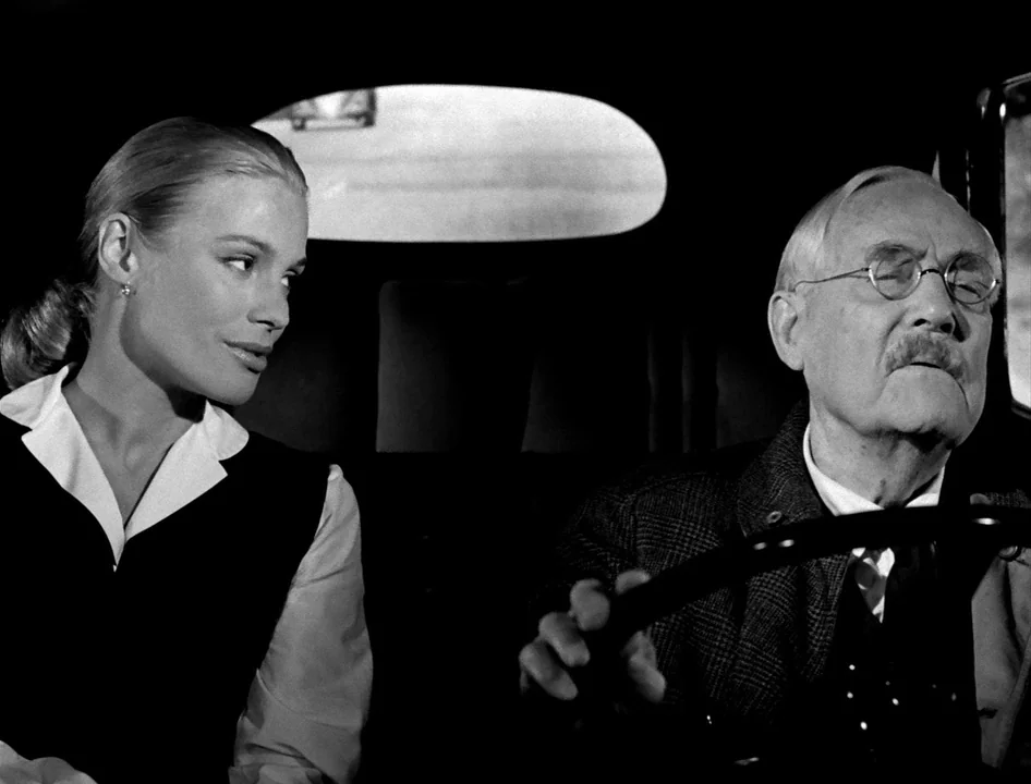 Wild Strawberries (1957) movie still: medium — The interior of a car shows a blonde woman sitting next to a driver. The elderly man drives with his…