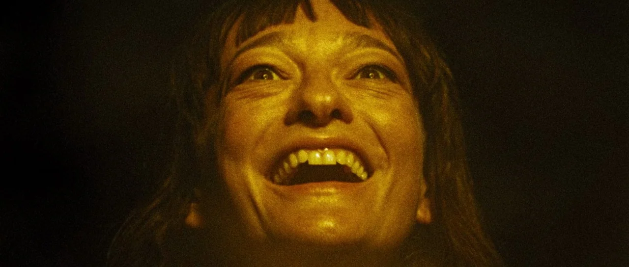 Let The Corpses Tan (2017) movie still: closeup — A dark, unidentifiable space surrounds the head and shoulders of a woman. She looks upward with…