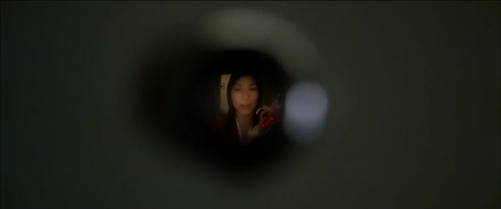 Kill Bill Vol. 2 (2004) movie still: closeup — The view is restricted to a circular peephole looking out at a hallway area. A young woman stands in…