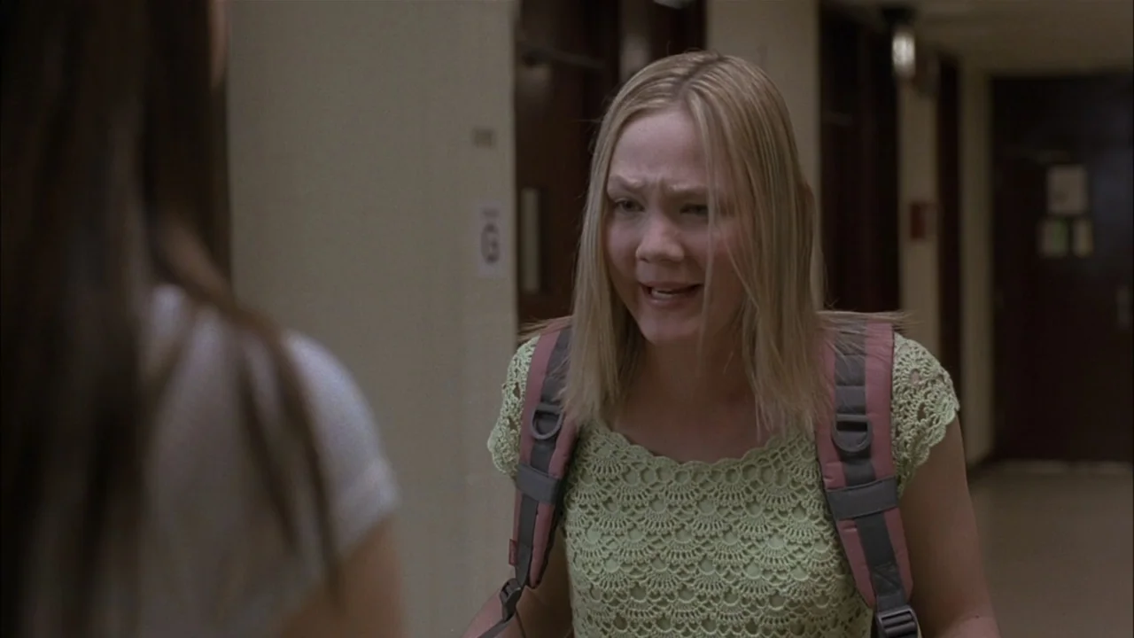 The Babysitters (2008) movie still: medium — A beige school hallway features locked doors and institutional walls with a small sign. A blonde woman…