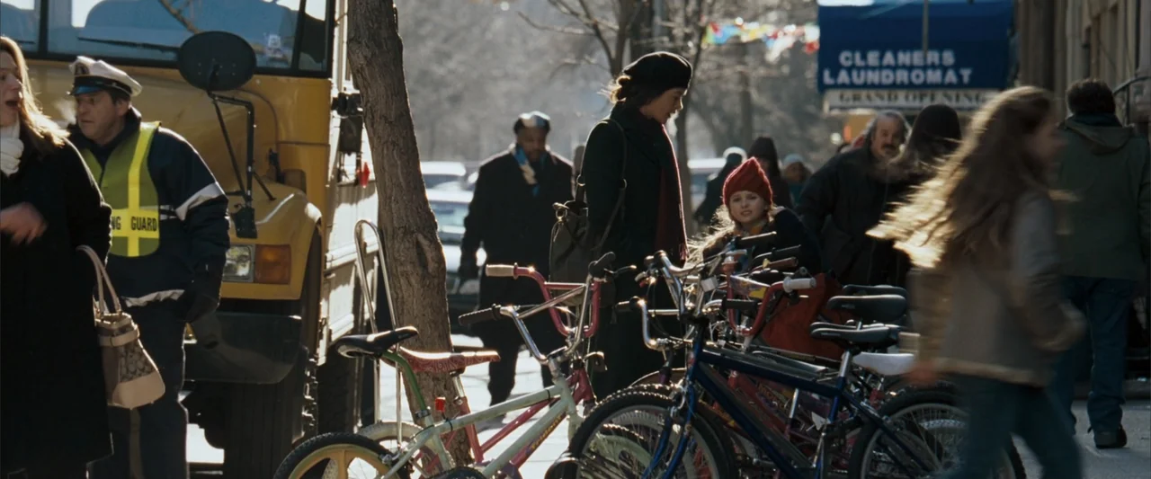 No Reservations (2007) movie still: medium — A sunny city street corner features a laundromat sign and parked bicycles on the sidewalk. A woman in a…