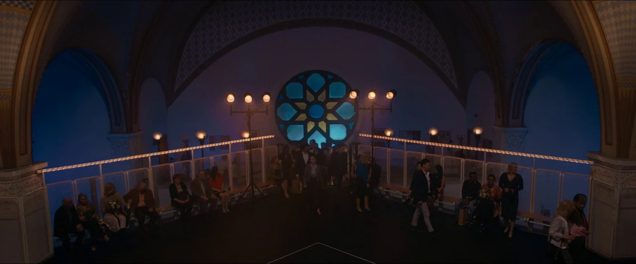 Birds of Paradise (2021) movie still: wide — A grand, vaulted indoor hall with stone arches features a large, central circular window. Numerous…