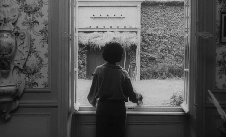 The Wild Child (1970) movie still: medium — An interior room with patterned wallpaper overlooks an outdoor courtyard with a thatched structure. A…