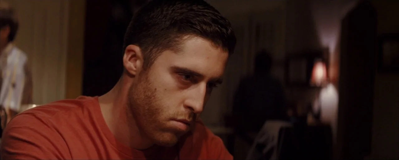 Krisha (2015) movie still: closeup — A dimly lit indoor space with shadows obscuring the background. A man looks down at something off-screen while…