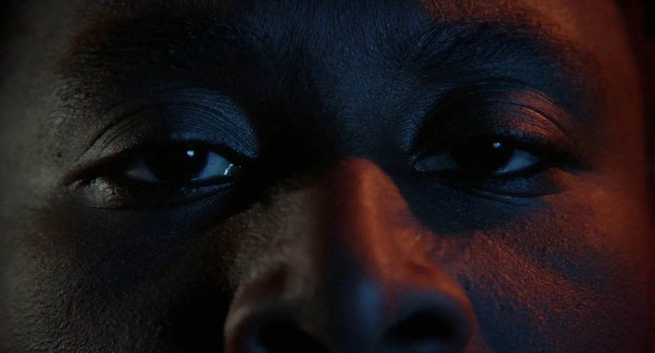 Def By Temptation (1990) movie still: closeup — A dark, nondescript interior space surrounds the subject. A person stares forward with intense focus…