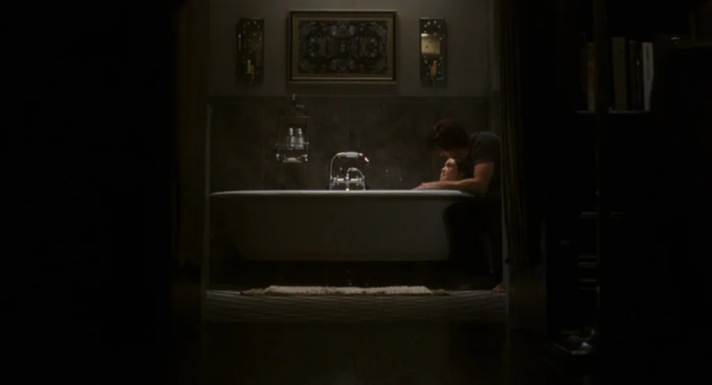 The Fountain (2006) movie still: wide — A dimly lit room with a white claw-foot tub against a tiled wall. A man sits on the edge of the tub looking…