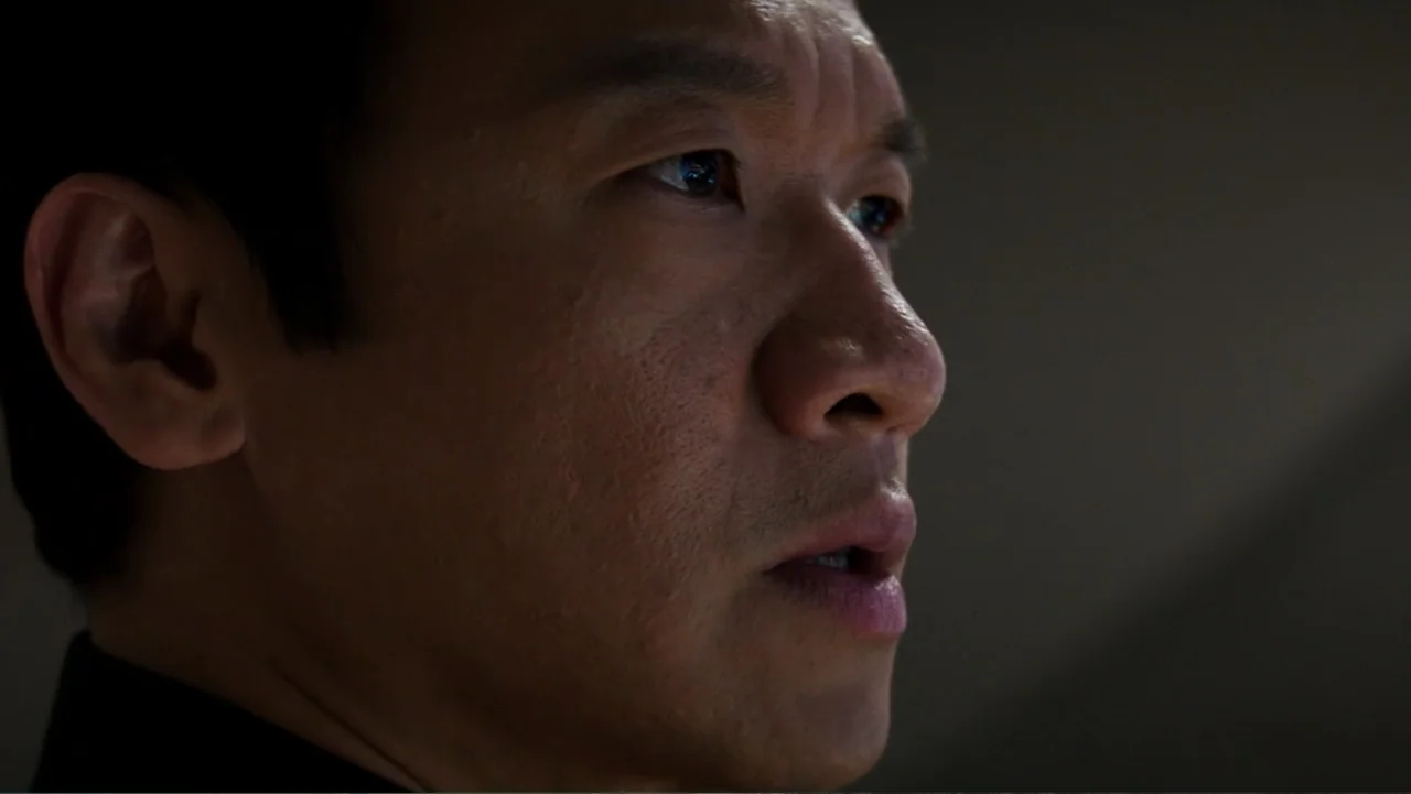 Skyscraper (2018) movie still: closeup — An interior space with dim lighting focused on a man's face. A man in his 40s faces three-quarter towards…