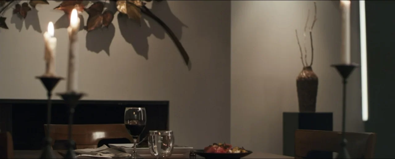 Hostages (2017) movie still: medium — A dining table features place settings with wine glasses and plates under candle illumination. The background…