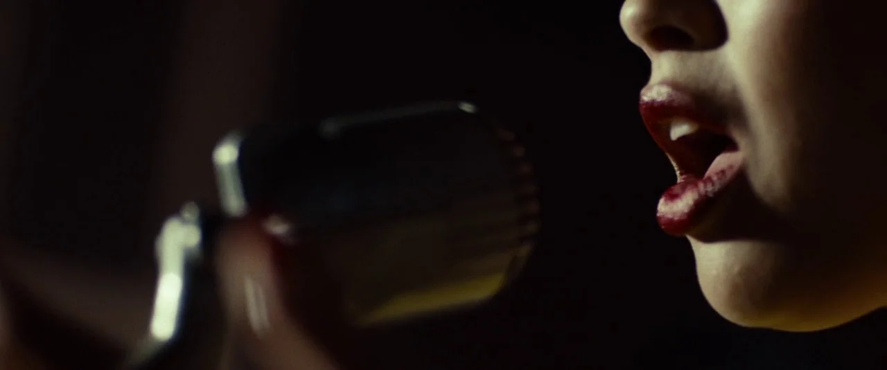 Kill Your Darlings (2013) movie still: closeup — A dark space with a microphone positioned directly in front of a person. A person with dark lips…