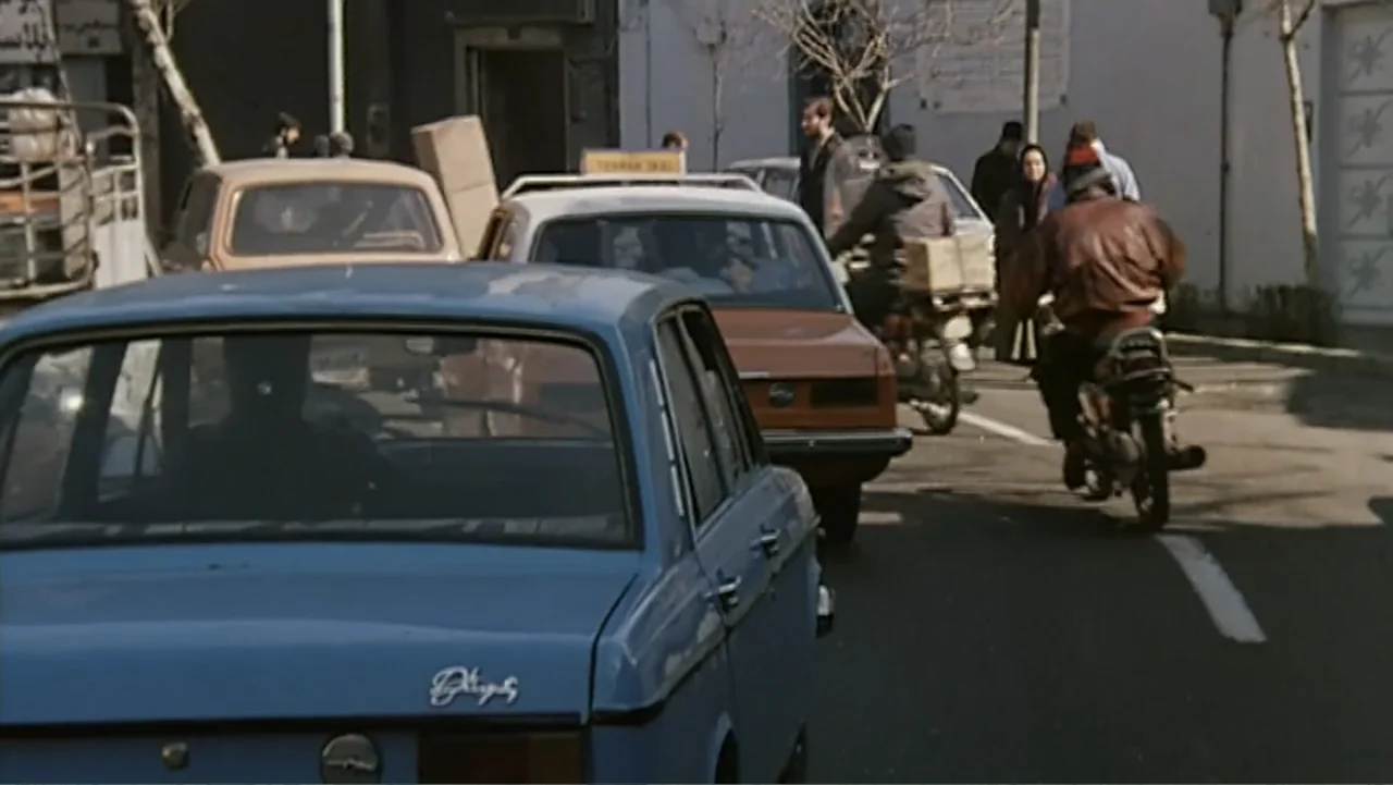 The Mirror (2014) movie still: medium — A busy city street in Tehran features several automobiles and a motorcycle in transit. A man on a motorcycle…