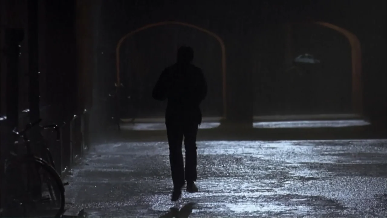 Starter for 10 (2006) movie still: fullbody — An outdoor stone arcade illuminated by faint lights at night with heavy rainfall visible. A lone…