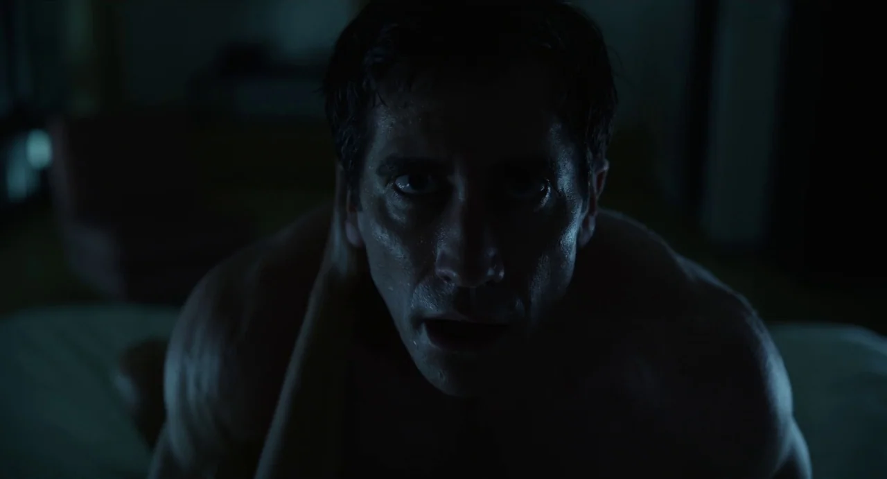 Velvet Buzzsaw (2019) movie still: closeup — A dark, dimly lit bedroom at night with minimal ambient light. A muscular man stares intensely toward…
