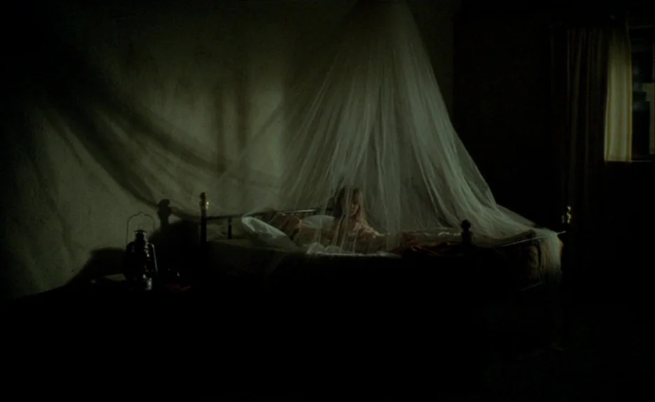 Chocolat (1988) movie still: wide — A dark, spartan room features an iron-framed bed draped in sheer, conical netting. A young girl rests in the…