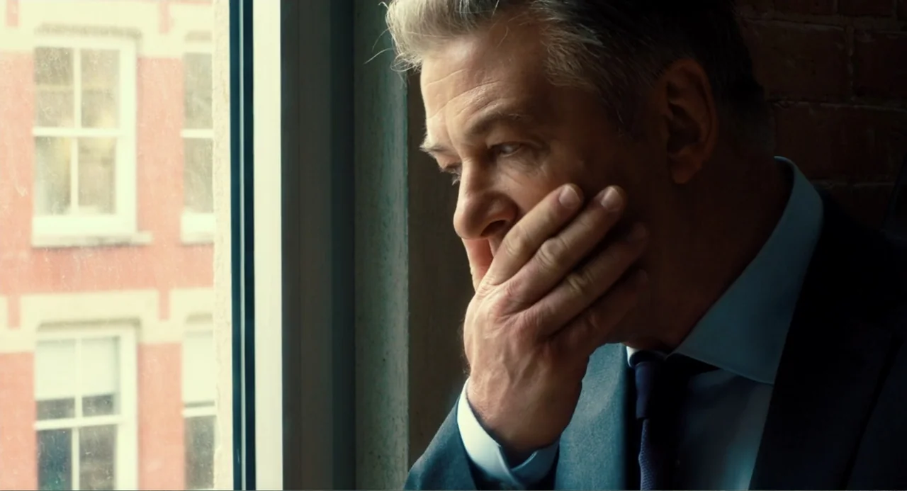 An Imperfect Murder (2017) movie still: closeup — An office interior features a large window overlooking a red brick building facade. A mature man…