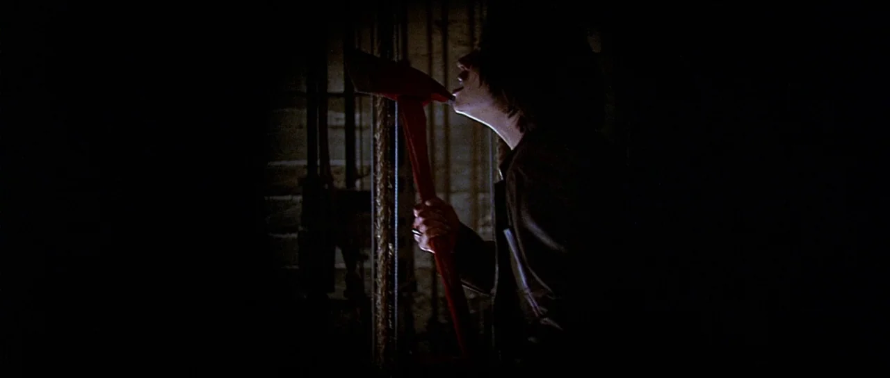 Scream 2 (1997) movie still: medium — A dimly lit, narrow space features vertical rope-like textures in the background. A woman in silhouette holds…
