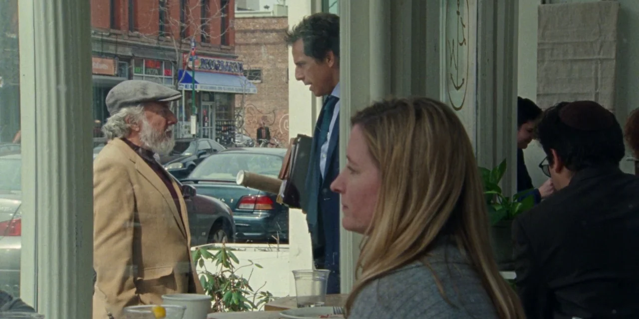 The Meyerowitz Stories (New and Selected) (2017) movie still: medium — An older man in a tan blazer stands outside a cafe entrance talking. A…