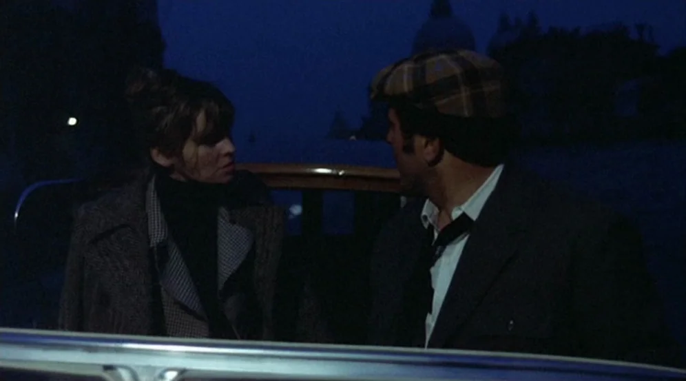 Don’t Look Now (1973) movie still: medium — A dark, dimly lit night scene inside a watercraft on a body of water. A man in a newsboy cap and a woman…