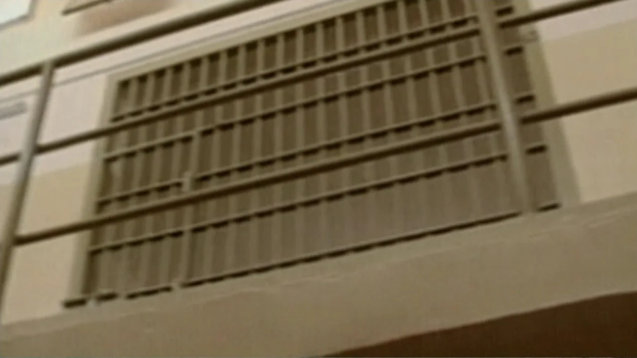 Ghosts of Abu Ghraib (2007) movie still: establishing — A utilitarian institutional interior shows a beige concrete wall and a steel barred gate.…