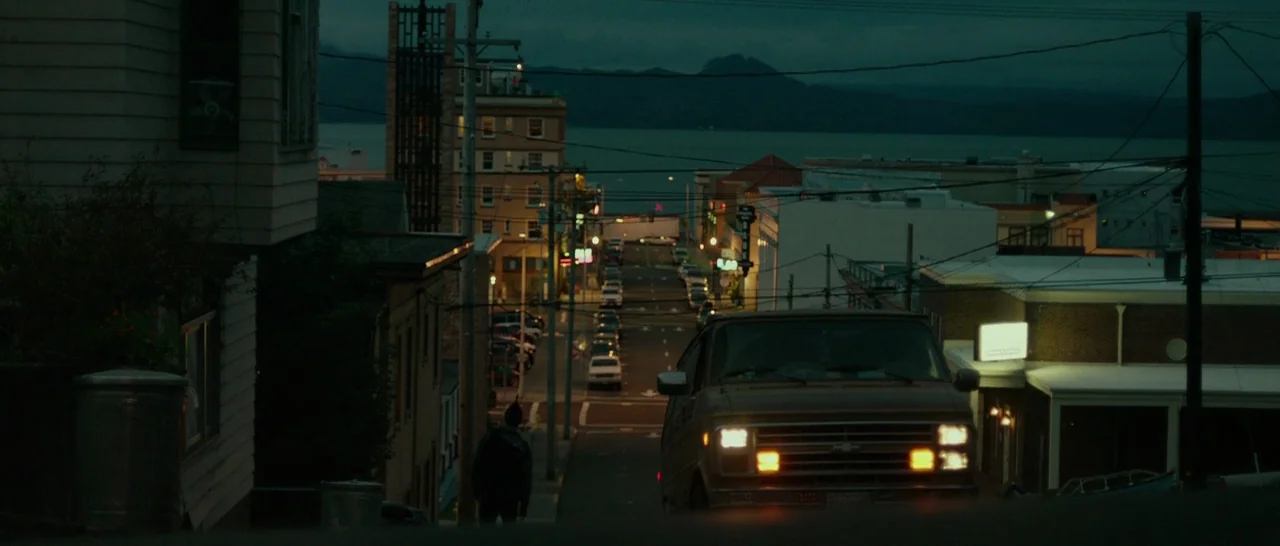 Green Room (2015) movie still: establishing — A quiet residential street at night features a lone figure walking away from camera. A brown van with…