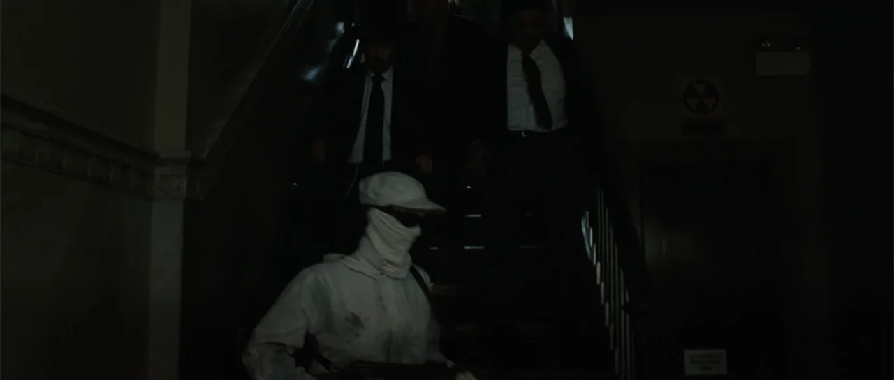 Inside Man (2006) movie still: medium — A dimly lit stairwell with wooden steps and shadows obscuring the background. Three men in professional and…