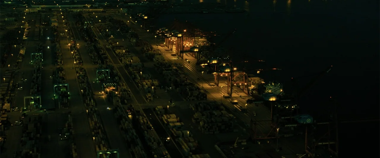 Den of Thieves 2: Pantera (2025) movie still: establishing — A vast shipping container terminal at night seen from a high aerial perspective. Rows…