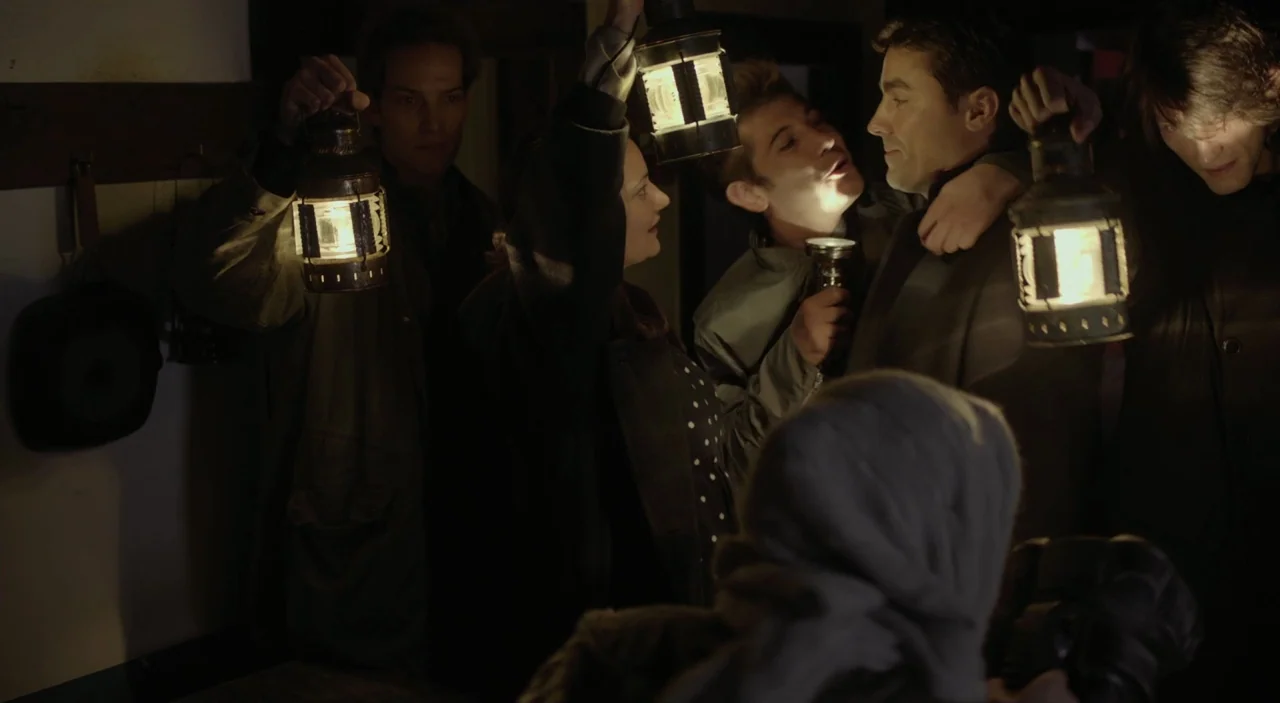 Cosmos (2015) movie still: medium — A group of five people crowd together in a dark room holding lit lanterns. They observe one another in the…