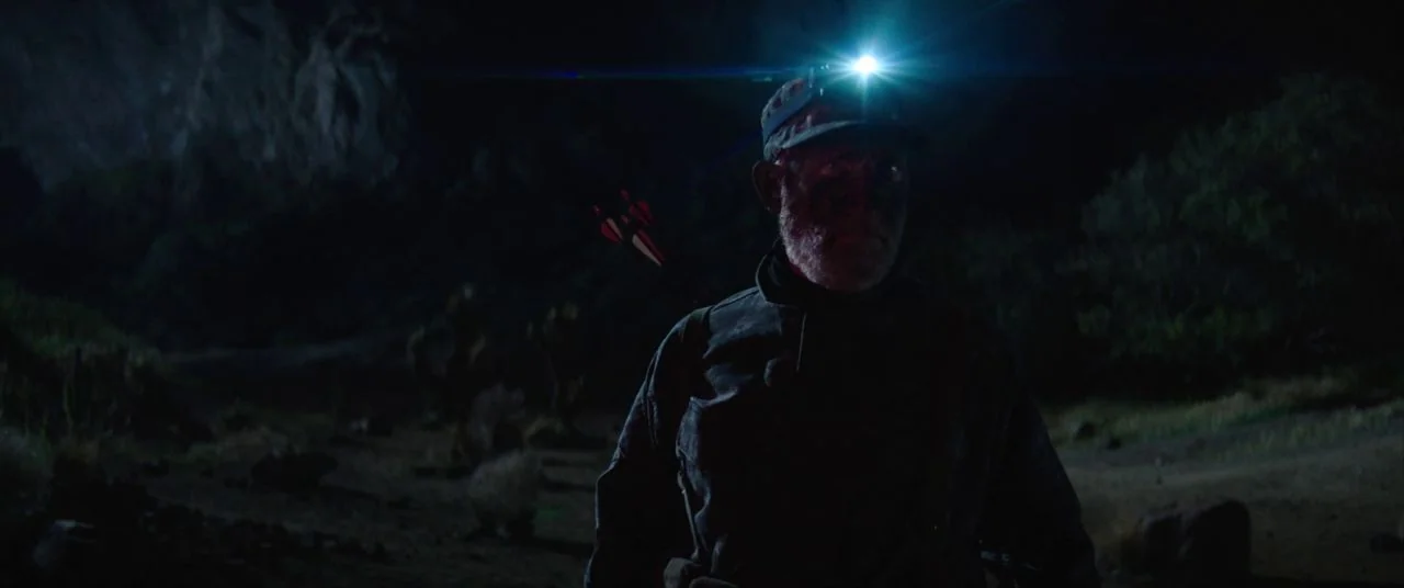 Palm Springs (2020) movie still: medium — A man stands in a dark, sparse desert environment at night. He is illuminated by a single, powerful…