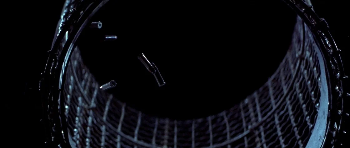 Carlito’s Way (1993) movie still: closeup — The interior of a metallic mesh cylinder is framed against a solid black background. Multiple spent…
