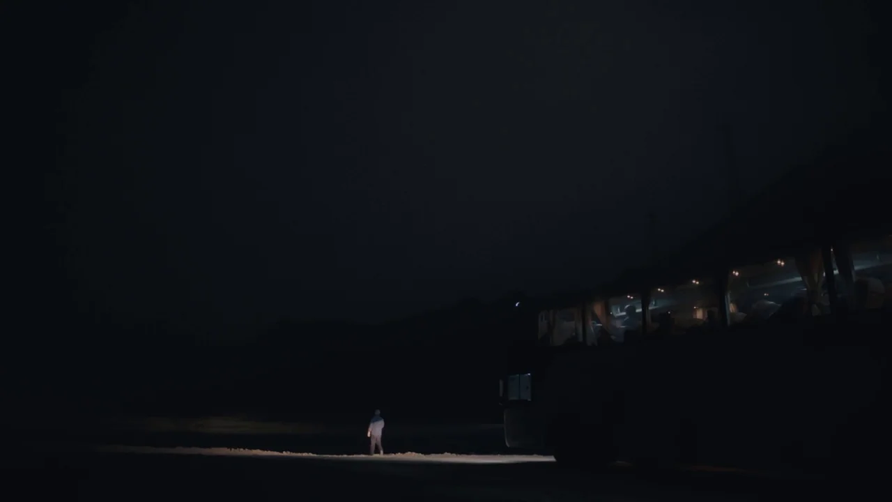 An Elephant Sitting Still (2018) movie still: wide — A dark night landscape shows a single bus parked on a desolate roadside area. A lone individual…