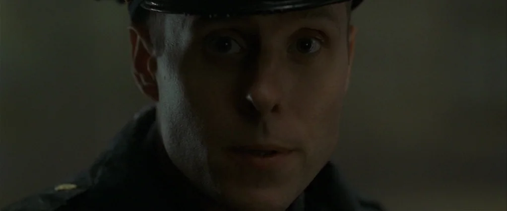 Panic Room (2002) movie still: closeup — A man in a dark police uniform stands in a dark outdoor setting at night. He stares ahead into the camera…