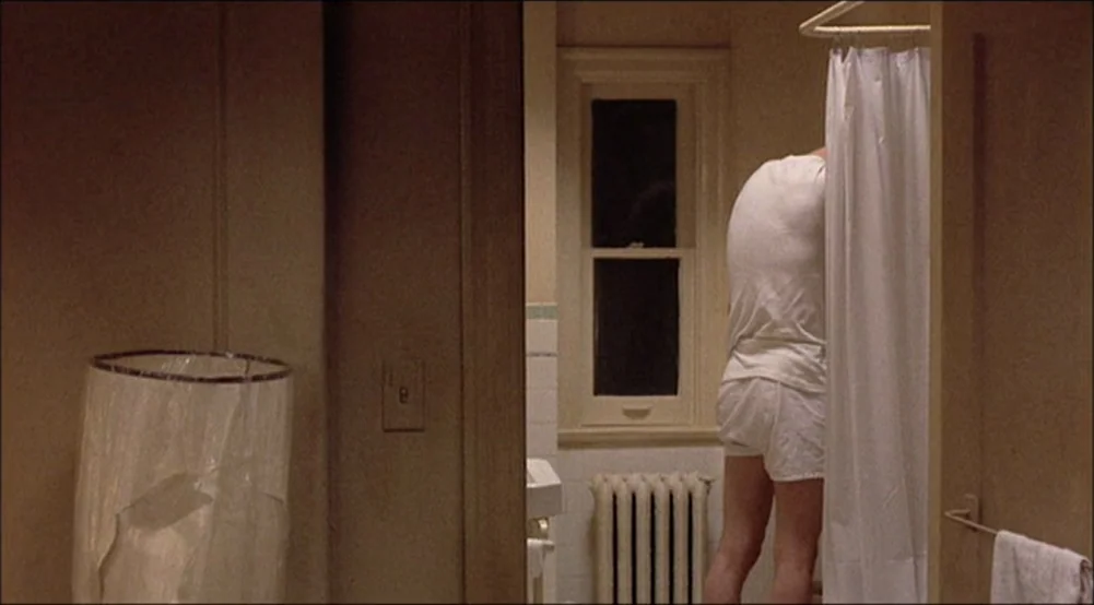 The Last Detail (1973) movie still: medium — An aging bathroom features beige walls and a window above a cast iron radiator. A man wearing white…