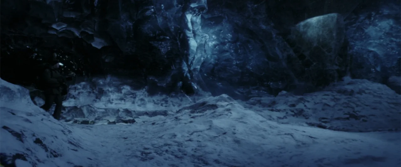 The Tomorrow War (2021) movie still: wide — A vast, dark ice cave with towering walls of frozen water and snow. A solitary individual in winter gear…