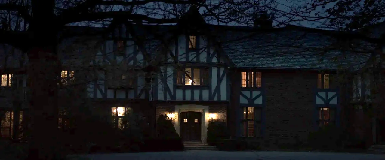 You’re Next (2013) movie still: establishing — A dark two-story Tudor-style mansion is silhouetted against the night sky. Light emanates from a few…
