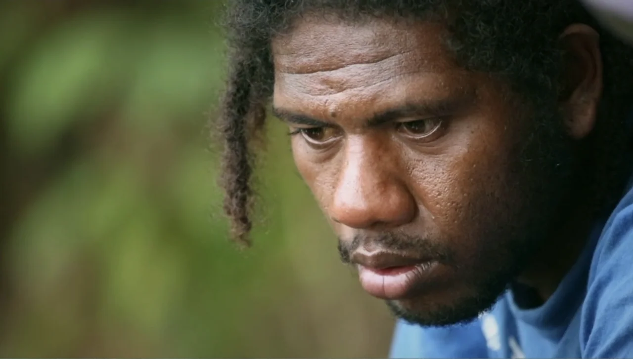 Islands of Creation (2015) movie still: closeup — An outdoor location with blurred green foliage visible in the out-of-focus background. A man looks…