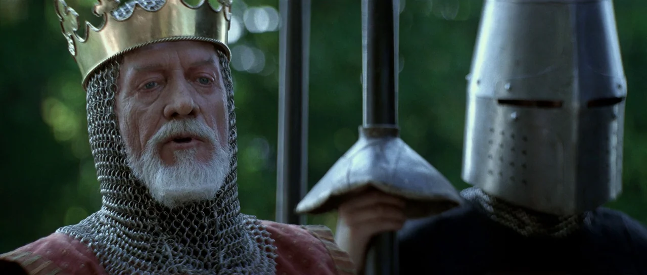 Braveheart (1995) movie still: medium — An elderly king in a crown and a knight in a helmet stand together. The background consists of out-of-focus…
